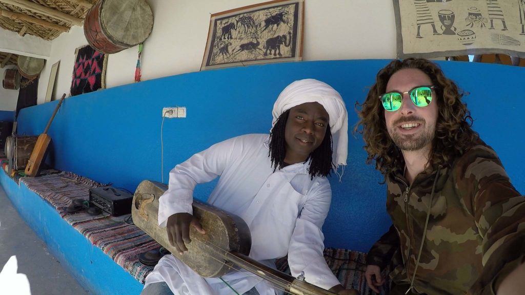 Abdoul187 en Kroon maken gnawa muziek op hun gimbri terwijl ze op een felblauwe bank zitten