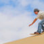 Een sandboarder zet af waardoor het zand achter haar opstuift