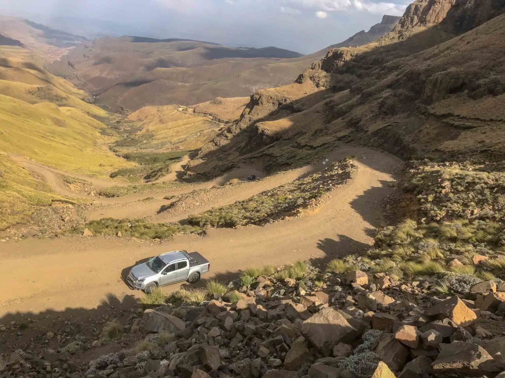 Een zilvere auto rijd de Sani Pass op met vele haarspeld bochten achter zich