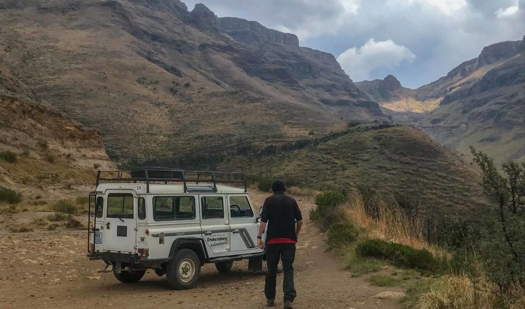 Een witte 4x4 staat stil op de Sani Pass. In de verte lopen de groen gele bergen omhoog