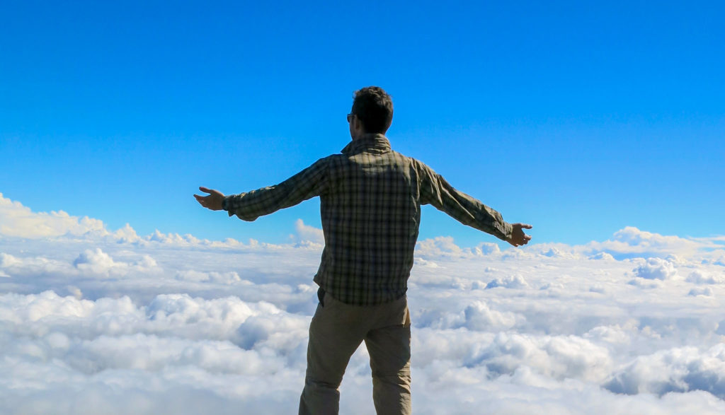 Een Kilimanjaro beklimmer staat bovenop de berg terwijl hij over de wolken uitkijkt.