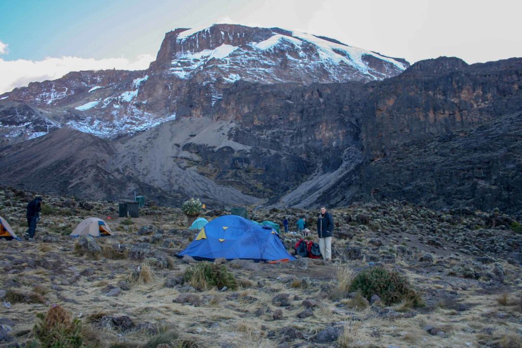 Een blauwe tent staat aan de voet van een rotsachtige wand op de Kilimanjaro