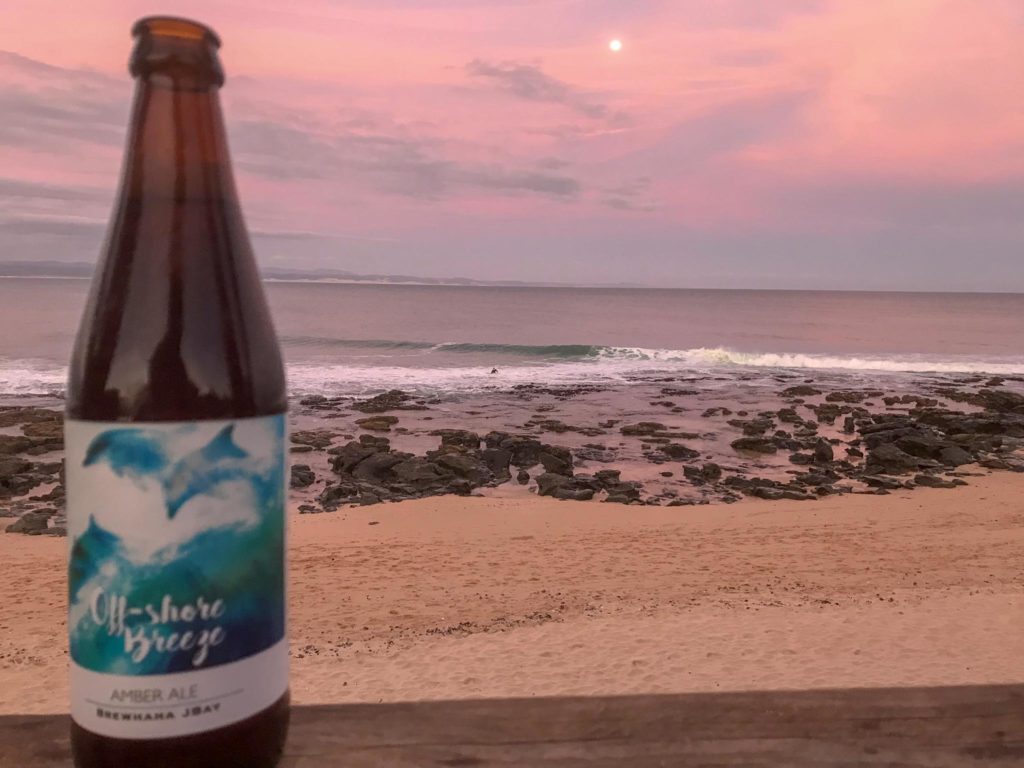 Een brewhaha op de voorgrond met het strand en de zee van Jeffreys Bay op de achtergrond