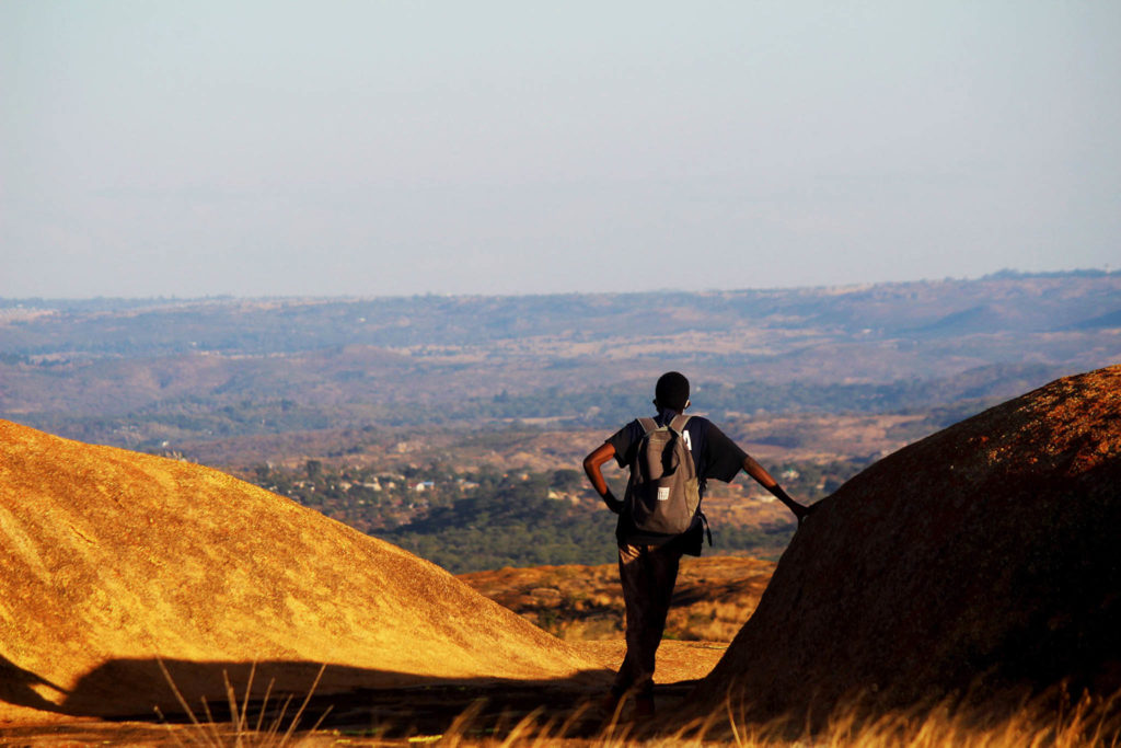 Een man leunt tegen de heuvels van Domboshava aan terwijl hij het uitzicht in zich op neemt