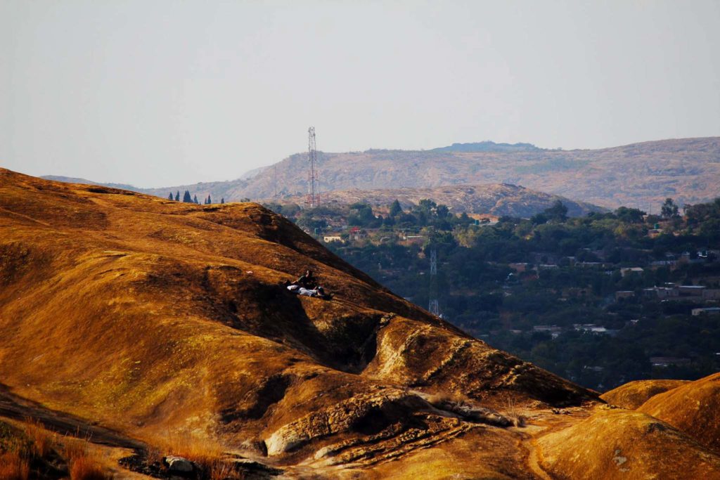 De goudbruine heuvels strekken ver en hoog, met op de achtergrond wat bebouwing in de verte.