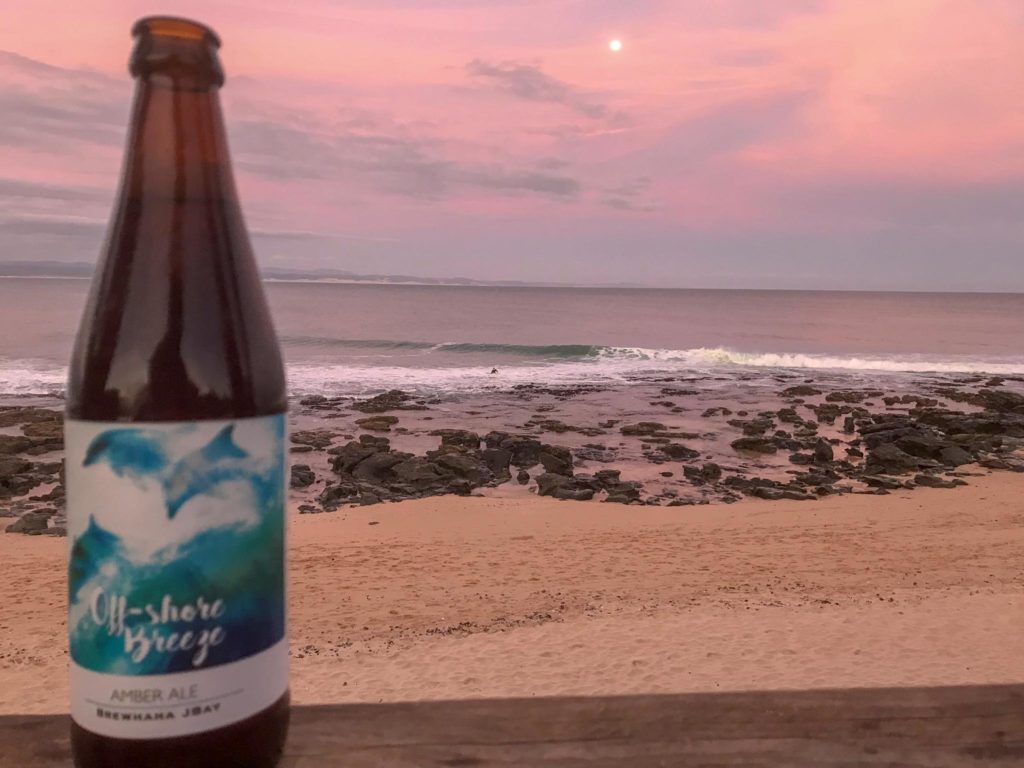 A brewhaha bottle in front of the beach and sea while the sun sets