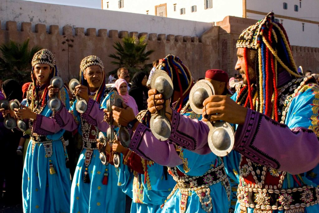 Vier Gnoaoua spelers lopen met hun instrumenten door de straat op het Gnawa Festival, één van de mooiste festivals in Marokko 