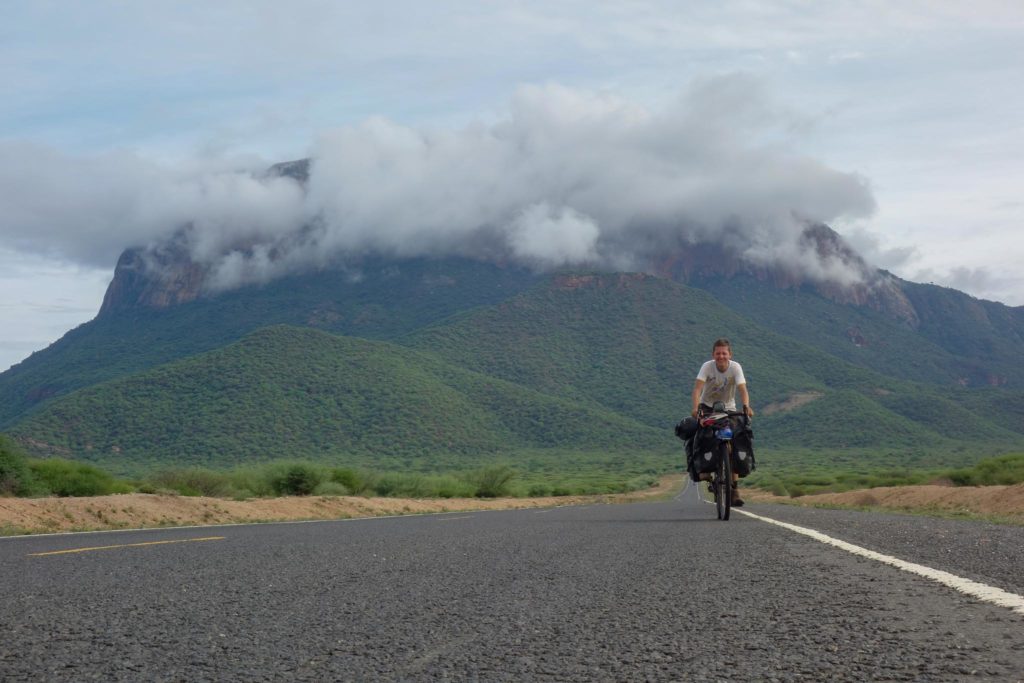 Niels op de fiets, met een grote groene berg vlak achter hem