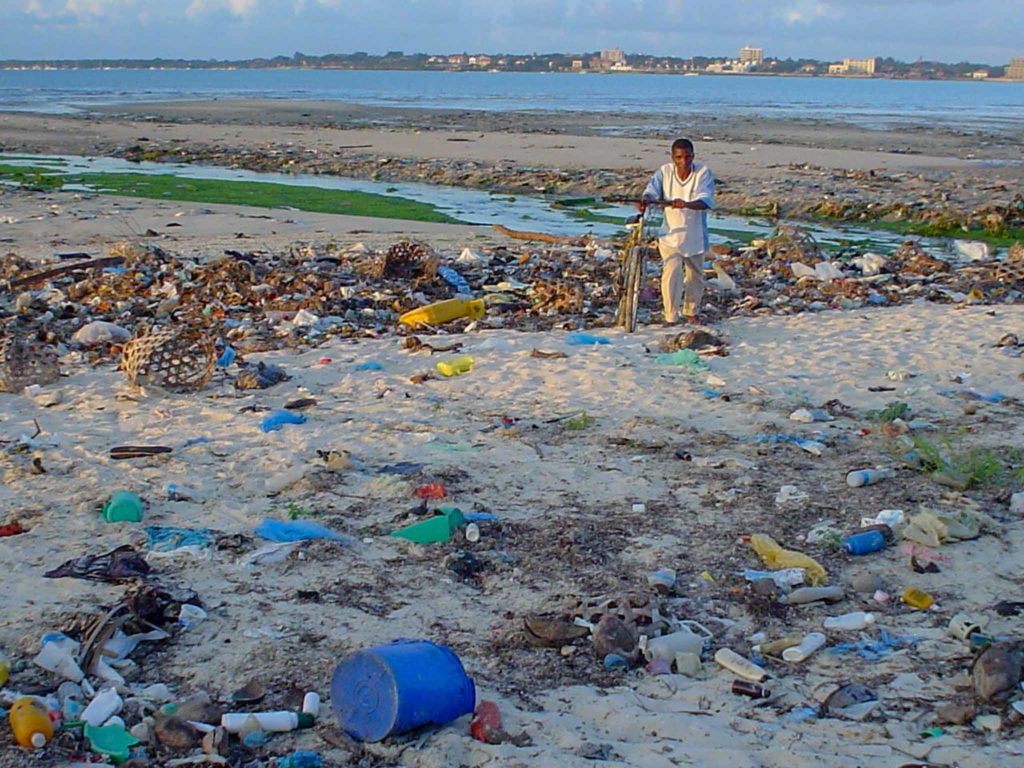 A man walks across a plastic littered beach in Tanzania