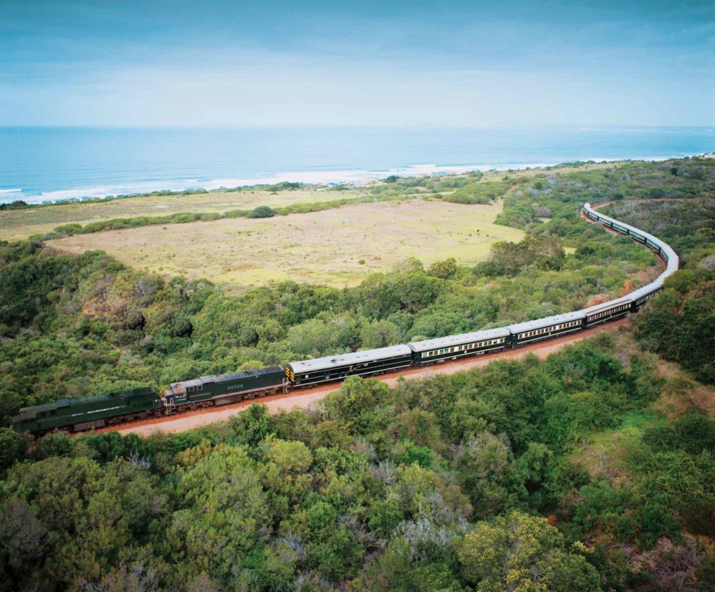 Een Rovos trein rijdt over het spoor in de Garden Rouge met de oceaan in de achtergrond.