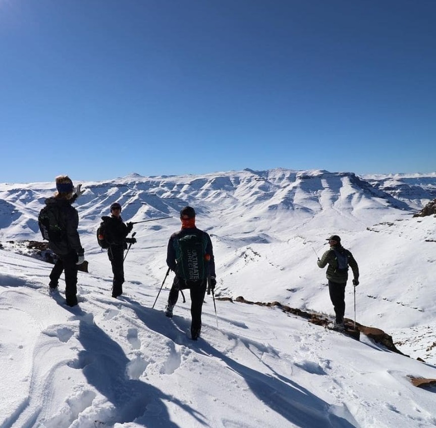 Vier hikers turen in de verte, waar het Drakensberg landschap bedolven is onder een dikke laag sneeuw.