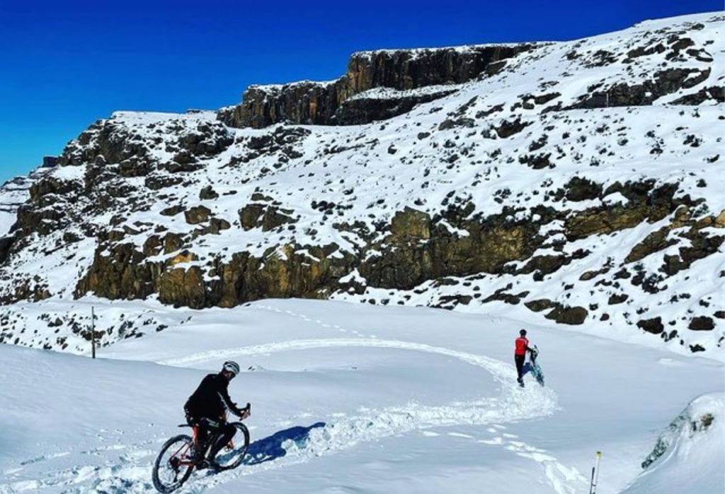 Twee fietsers gaan de besneeuwde Sani Pass af. De één probeert nog te fietsen terwijl de ander de fiets al aan de hand heeft.